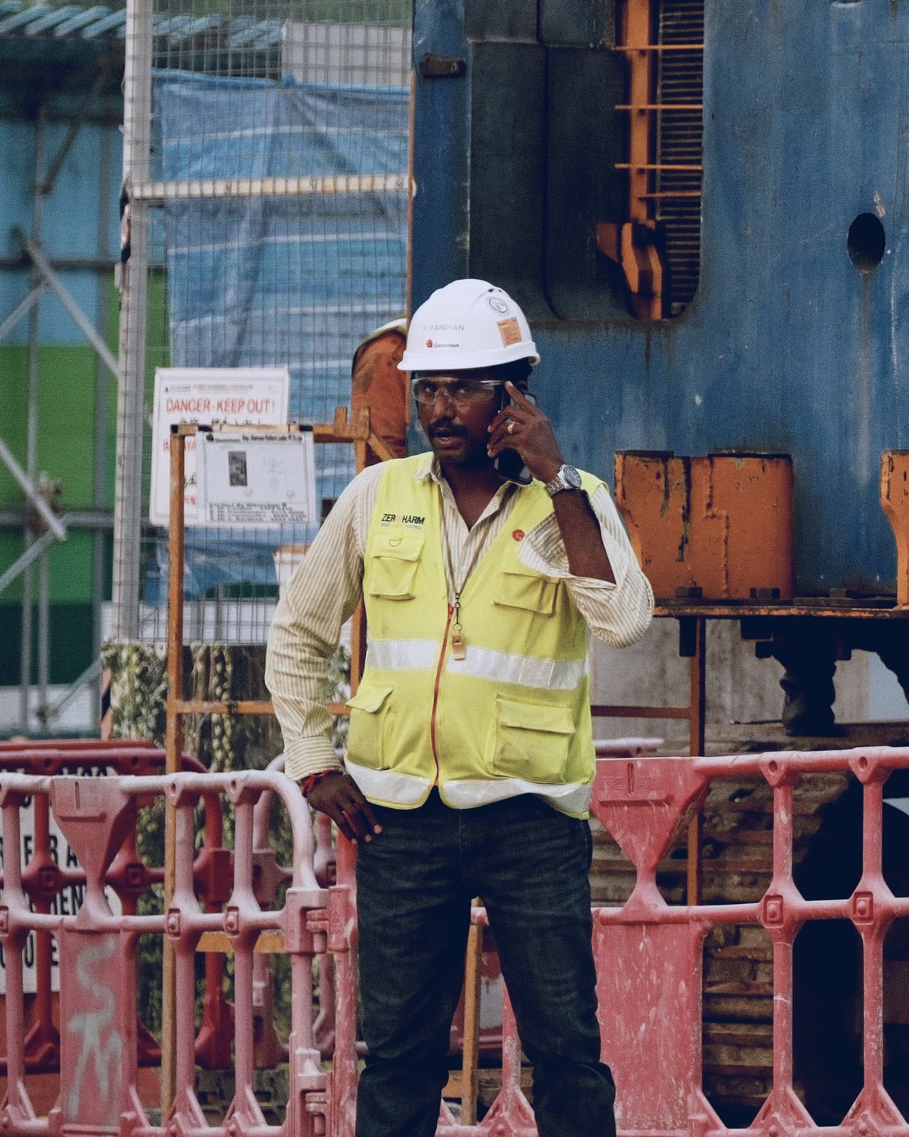 Site supervisor in a hard hat and hi-vis vest taking a call on site