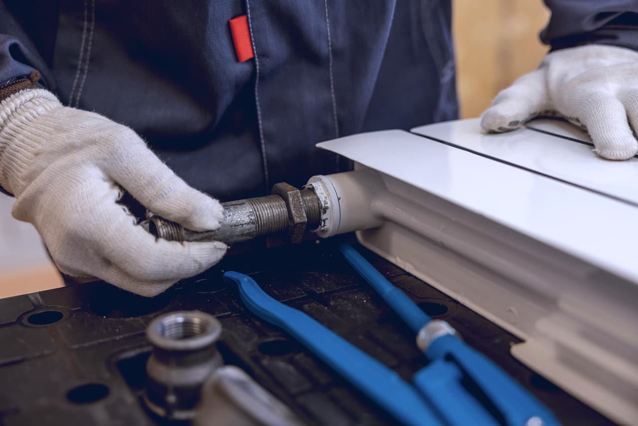 Heating engineer in work gloves fitting a radiator pipe